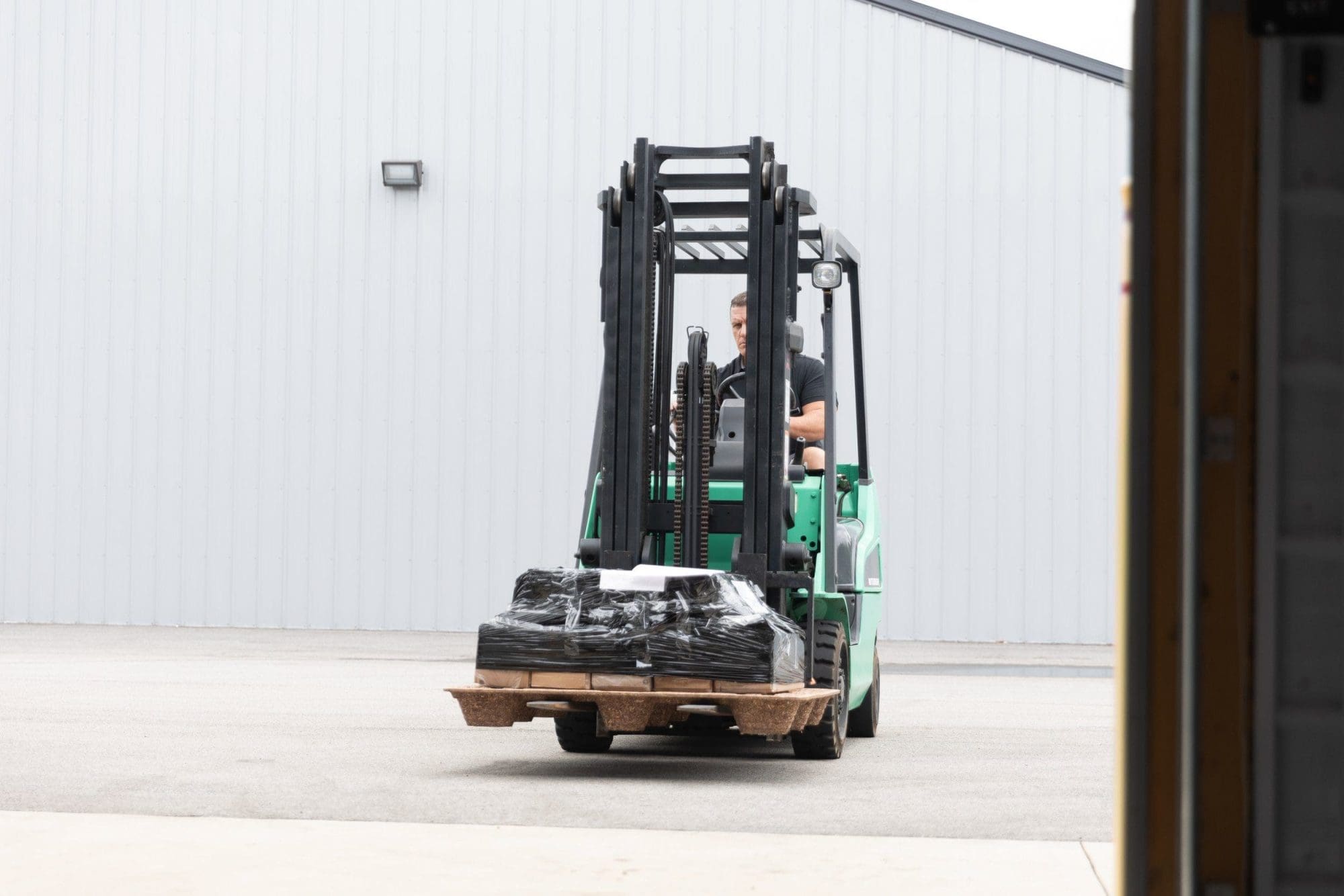 A man driving a green forklift outside of a storage area