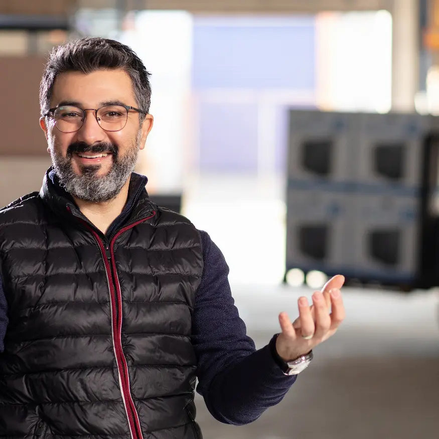 A man wearing glasses and a black vest, smiling as he explains something