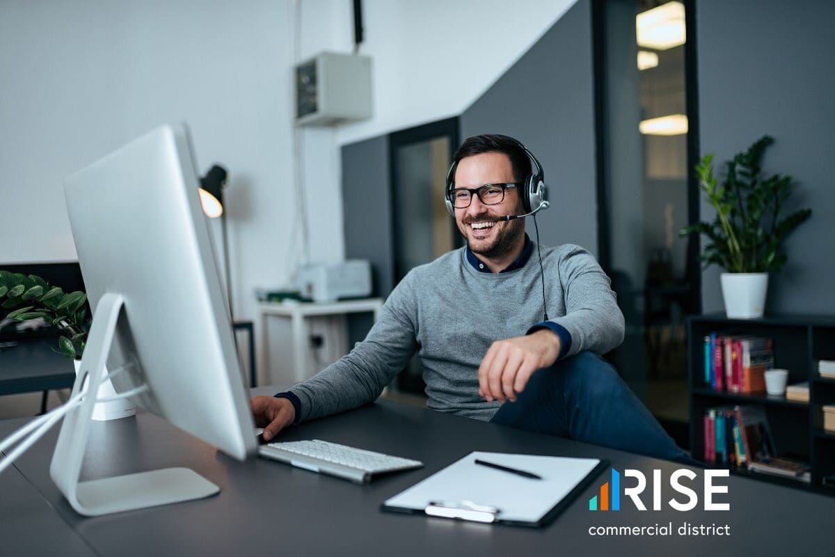 A man sitting at a desk, wearing a headset and smiling