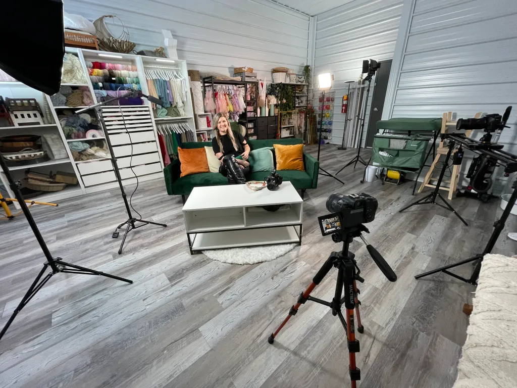 A woman sitting on a green couch in front of a camera in a business rental space